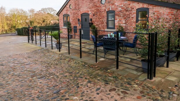 Un bâtiment en briques doté d’un patio dallé, d’un espace extérieur aménagé avec des sièges et d’une entrée fermée par un portail.