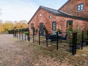 A brick building with a paved patio area, outdoor seating, and a gated entrance. - Grimsditch Dairy (Knutsford)