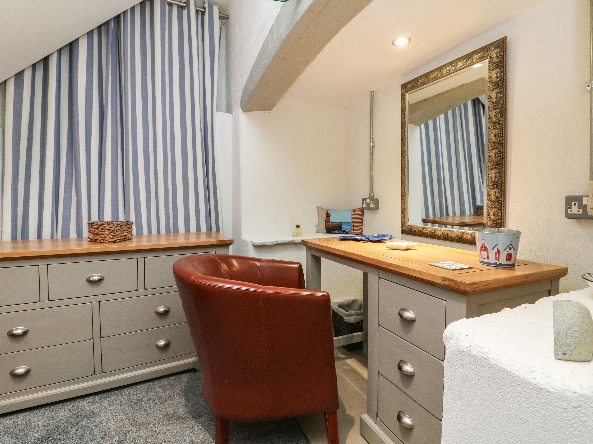 A hotel room with a wooden desk, a red chair, a large mirror, and striped curtains.