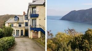 A coastal building with a staircase leading to a balcony, overlooking a body of water and a mountainous landscape. - Blue Bay (Lynton)