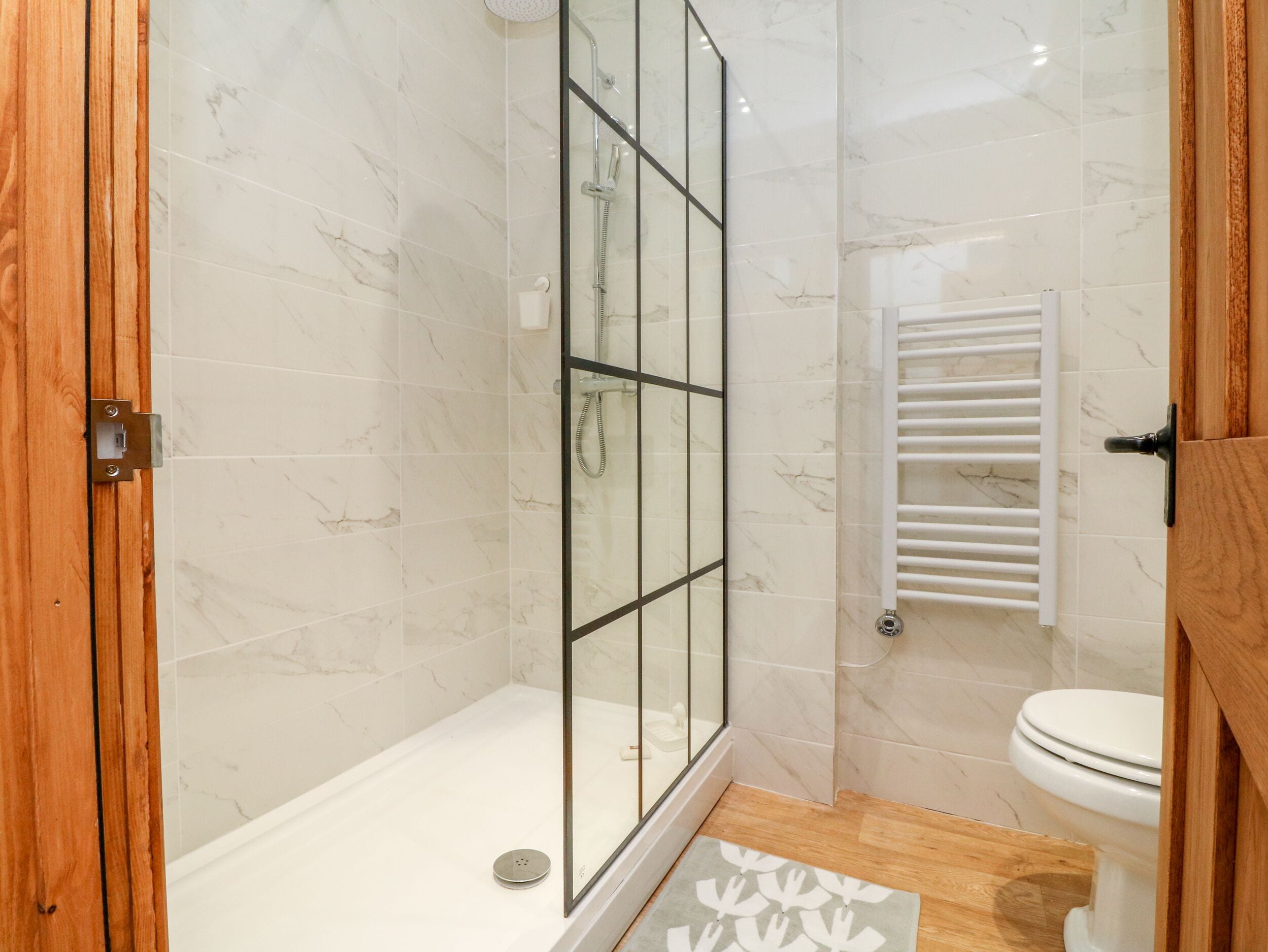 A bathroom with a glass-enclosed shower, a white toilet, and a wooden door.