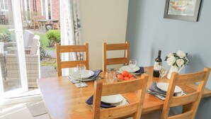 A dining table set for four with wooden chairs, a vase of white flowers, a bottle of wine, and a basket of oranges. - Blue Skye, 17 Talisker Walk (Filey)