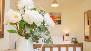 A room with a wooden bed, a white vase with white flowers, and a painting on the wall. - Blue Skye, 17 Talisker Walk (Filey)