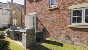 A brick house with a patio area featuring wicker furniture and a glass table. - Blue Skye, 17 Talisker Walk (Filey)
