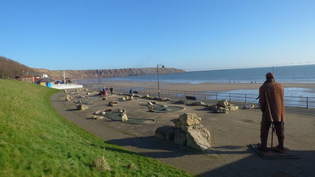 A coastal area with a large statue, a paved walkway, and a beach in the background. - Blue Skye, 17 Talisker Walk (Filey)