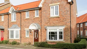 A two-story brick house with a red-tiled roof, a bay window, and a red door. - Blue Skye, 17 Talisker Walk (Filey)