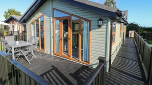 Une terrasse en bois avec une porte-fenêtre, une table avec des chaises et un petit espace extérieur.