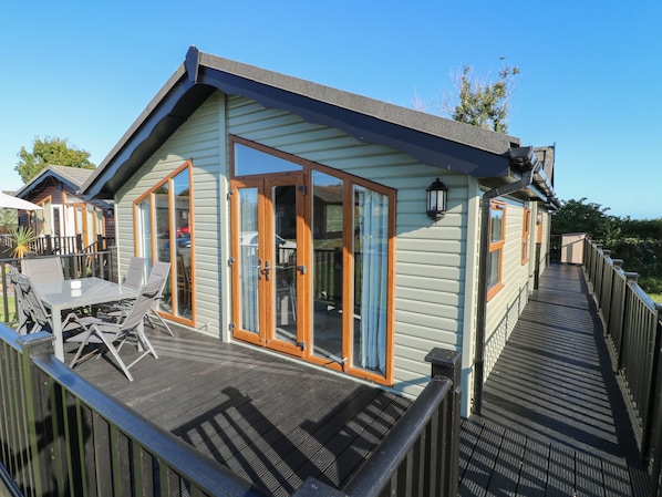 Une terrasse en bois avec une porte-fenêtre, une table avec des chaises et un petit espace extérieur.