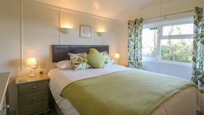 Une chambre à coucher comprenant un lit, des tables de chevet, une fenêtre avec des rideaux et un luminaire au plafond.