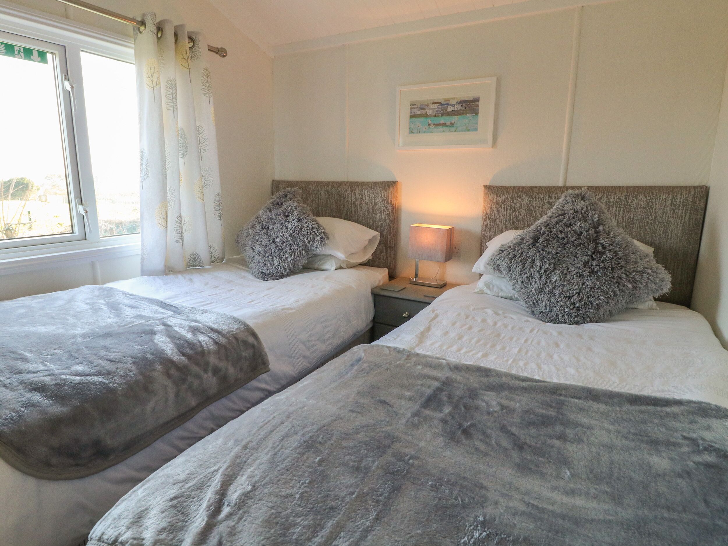 Een hotelkamer met twee bedden, een nachtkastje met lamp, een raam met gordijnen en een ingelijst schilderij aan de muur.