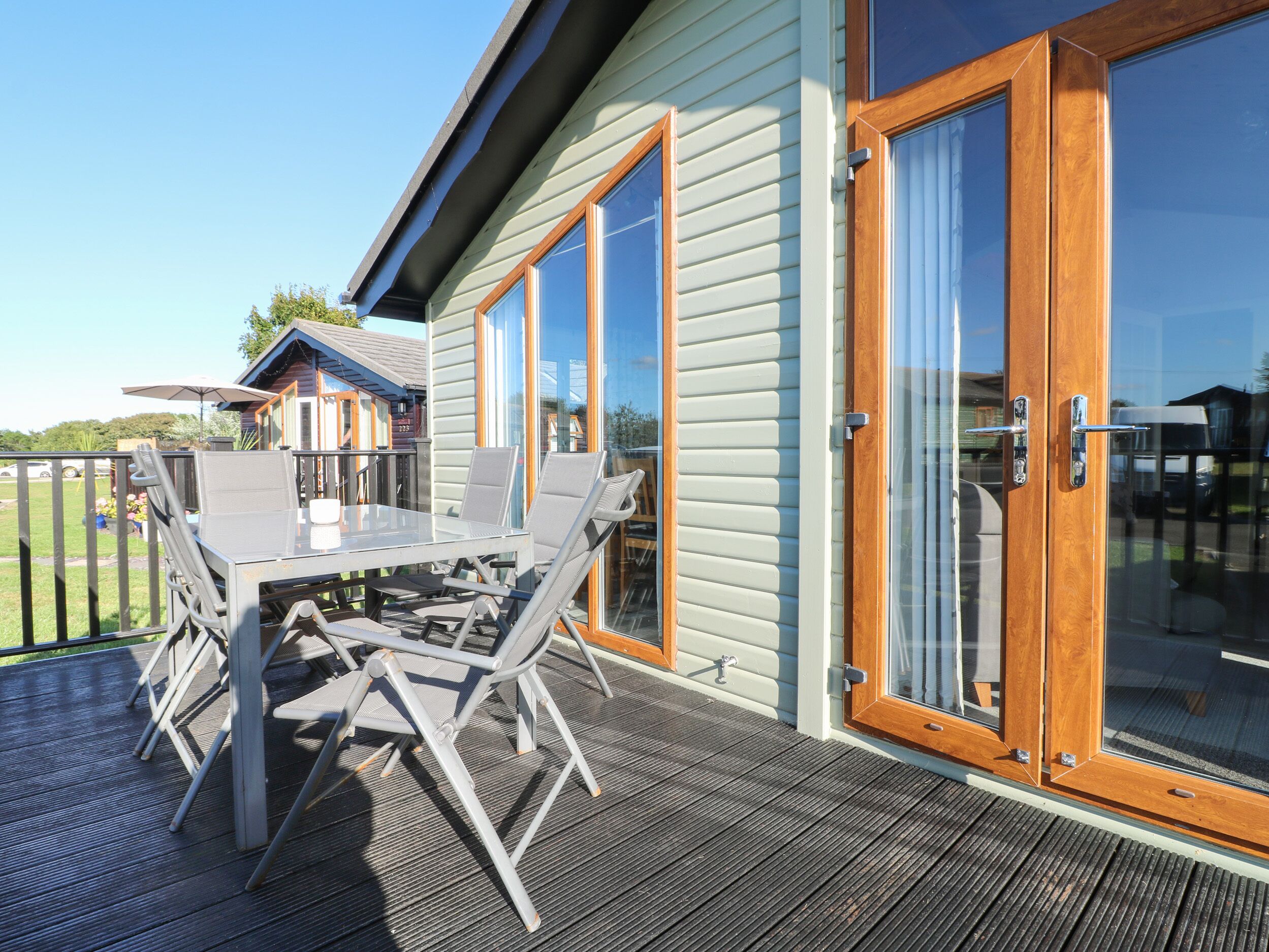 En terrasse med et bord og stole, en trædør med glasruder, og udsigt over det omkringliggende område.