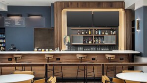 Una zona de bar con mostrador, taburetes y una variedad de botellas y vasos.