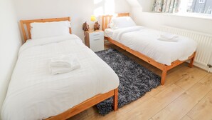Une chambre à coucher avec deux lits en bois, une literie blanche, une petite table de chevet avec une lampe, un tapis noir et un tableau accroché au mur.