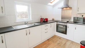 Une cuisine moderne avec des meubles blancs, un plan de travail noir, un puits de lumière, une hotte en acier inoxydable, un four à micro-ondes et une bouilloire rouge.