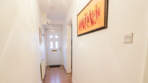 Un couloir au sol en bois, une porte blanche au fond et une œuvre d’art encadrée accrochée au mur.