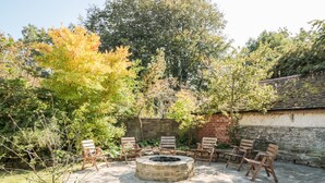 An outdoor patio with stone flooring, a circular fire pit, and wooden chairs arranged around it. - Carriage House (Presteigne)