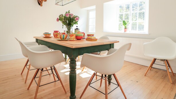 A dining area with a wooden table, white chairs, a vase with flowers, and a deer head mounted on the wall. - Carriage House (Presteigne)