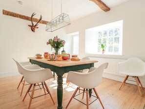 A dining area with a wooden table, white chairs, a vase with flowers, and a deer head mounted on the wall. - Carriage House (Presteigne)