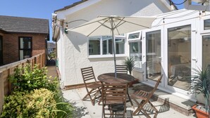 A patio with a table and chairs, a white umbrella, and potted plants. - Seagull Cottage (Holyhead)