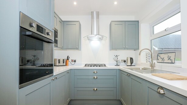 A modern kitchen with grey cabinets, a stainless steel oven, a gas stove, and a window with a view. - Seagull Cottage (Holyhead)
