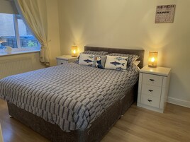 Un dormitorio ordenado con una colcha estampada, dos lámparas de noche y una decoración en la pared.