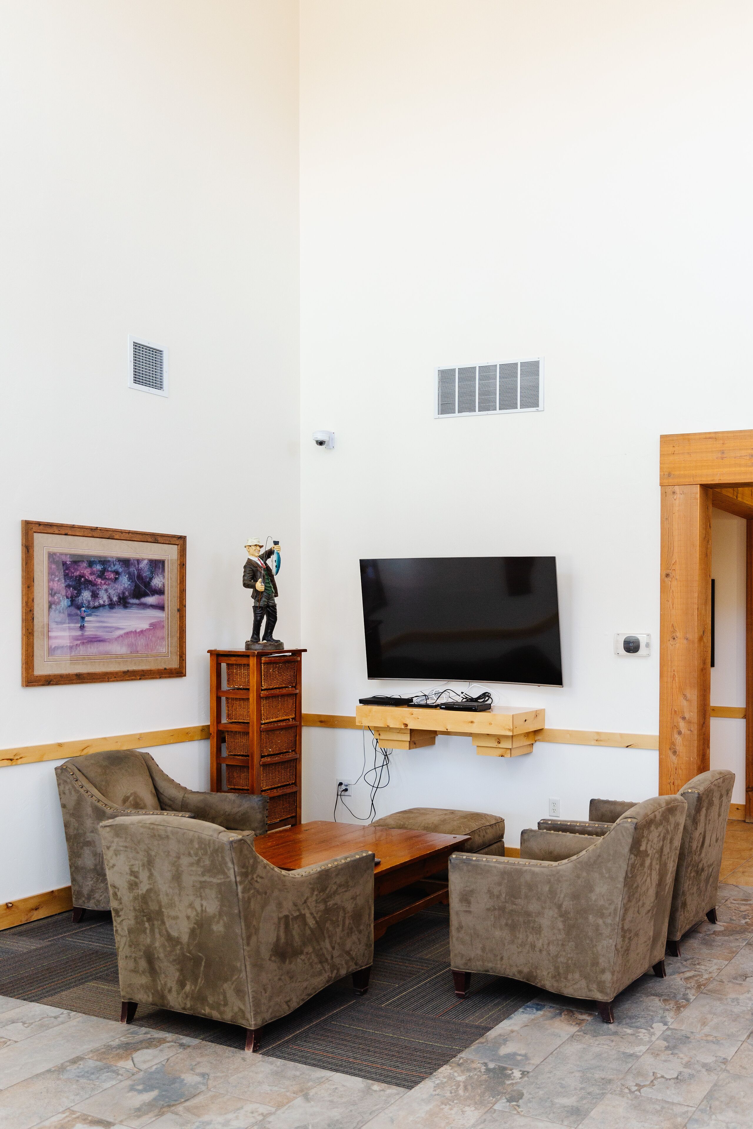Ein Wohnzimmer mit Flachbildfernseher, zwei Sesseln, einem Holztisch und einem gerahmten Gemälde an der Wand.