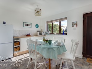 A kitchen with a dining table, chairs, a refrigerator, a microwave, and a window with a view of greenery. - Sea Views (Dorchester)