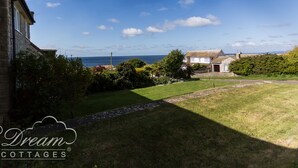 Une propriété située sur la côte, avec un bâtiment en pierre, une pelouse verdoyante et une vue sur la mer.
