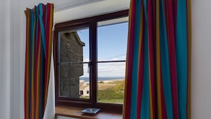 Une pièce dotée d’une fenêtre donnant sur un paysage, un mur en pierre et une vue sur la mer.