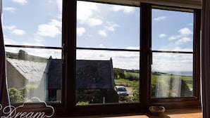 Une pièce dotée d’une grande fenêtre donnant sur un paysage rural, avec une maison et des champs.