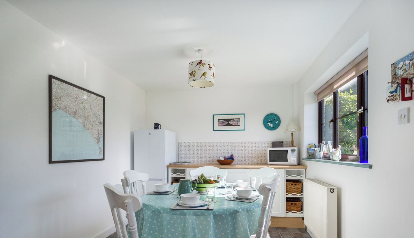 Cocina compacta con comedor, armarios blancos, salpicadero de azulejos, microondas y ventana con vistas.