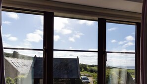 A room with a large window overlooking a rural landscape, including a house and fields. - Sea Views (Dorchester)