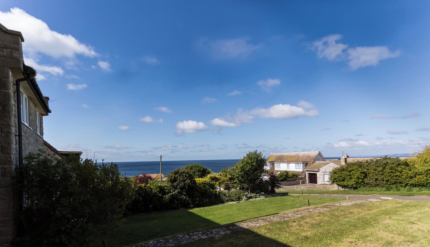 Une propriété située sur la côte, avec un bâtiment en pierre, une pelouse verdoyante et une vue sur la mer.