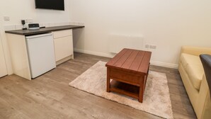 Un espacio habitable compacto con kitchenette, una mesa de madera, un sofá y un televisor montado en la pared.