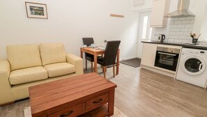 Una sala de estar moderna con un sofá, una mesa de centro de madera y una mesa de comedor con sillas. Hay una zona de cocina con estufa, horno y lavadora.
