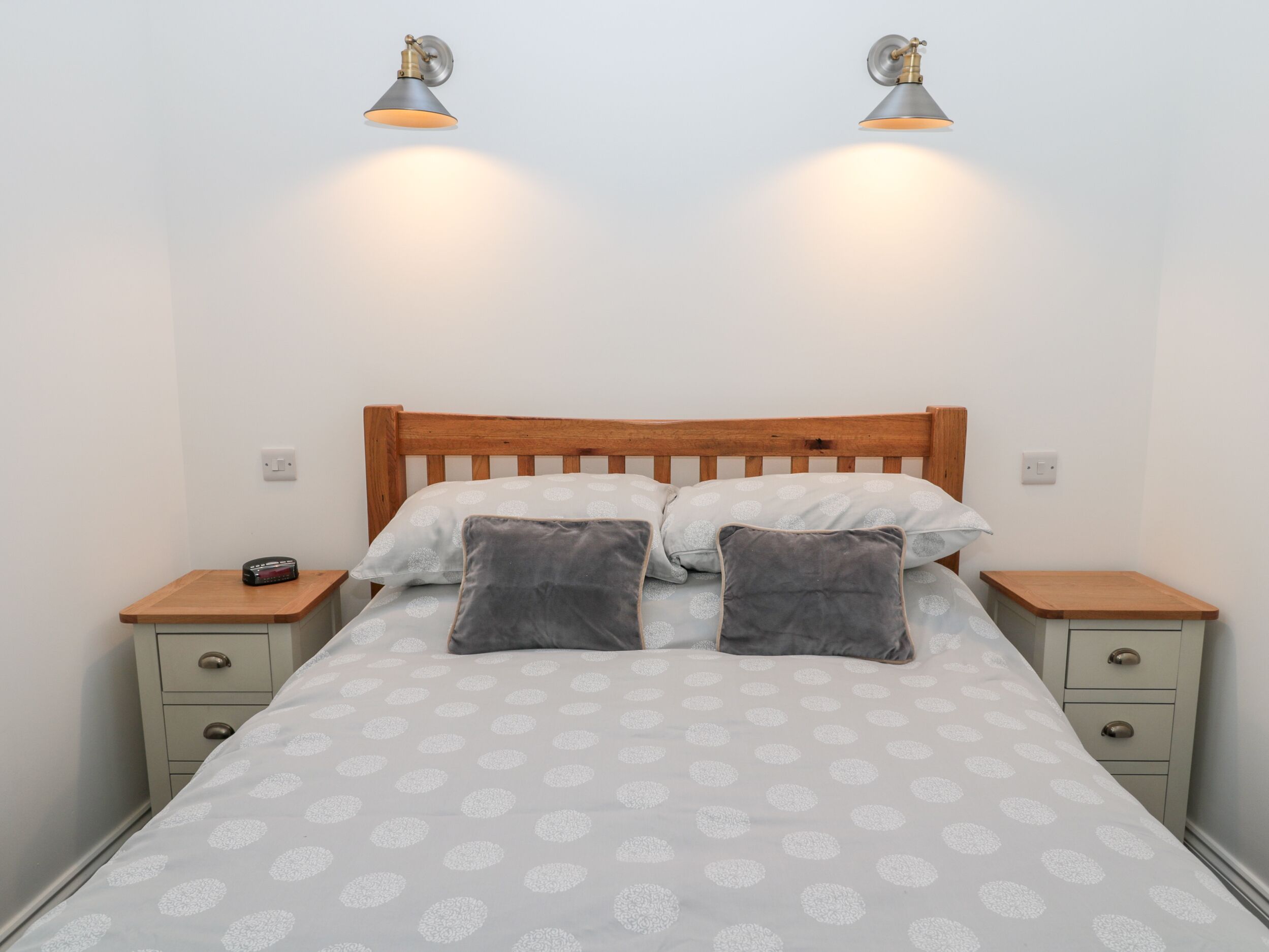 A bed with a wooden headboard, two bedside tables, and two wall-mounted lamps.