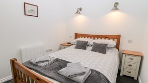 Una cama bien hecha con cabecera de madera, dos mesitas de noche, un cuadro enmarcado en la pared y dos lámparas fijadas a la pared.