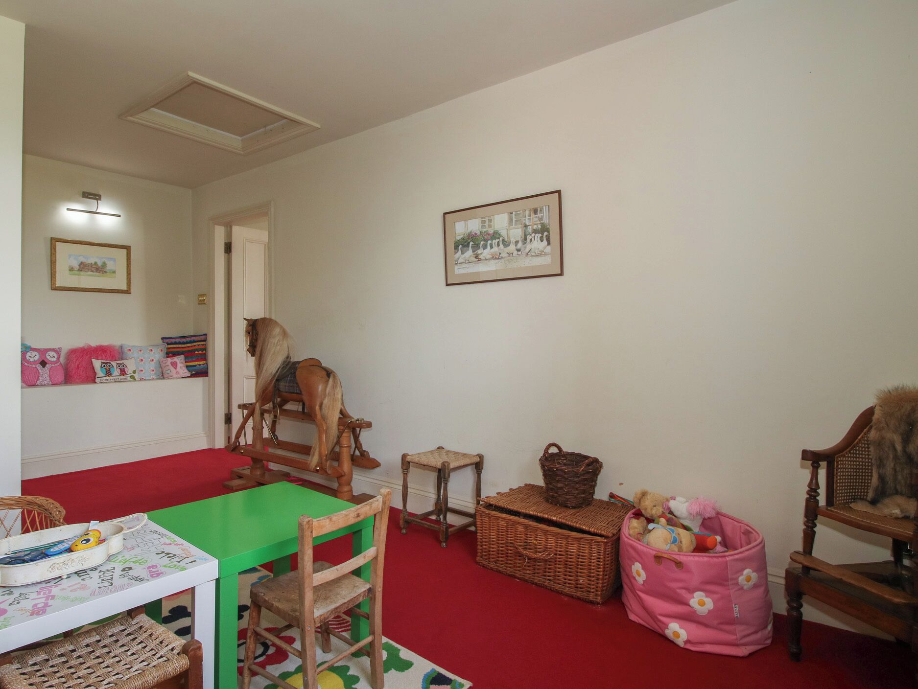 A room with a green table, a rocking horse, wicker baskets, and a pink bag.