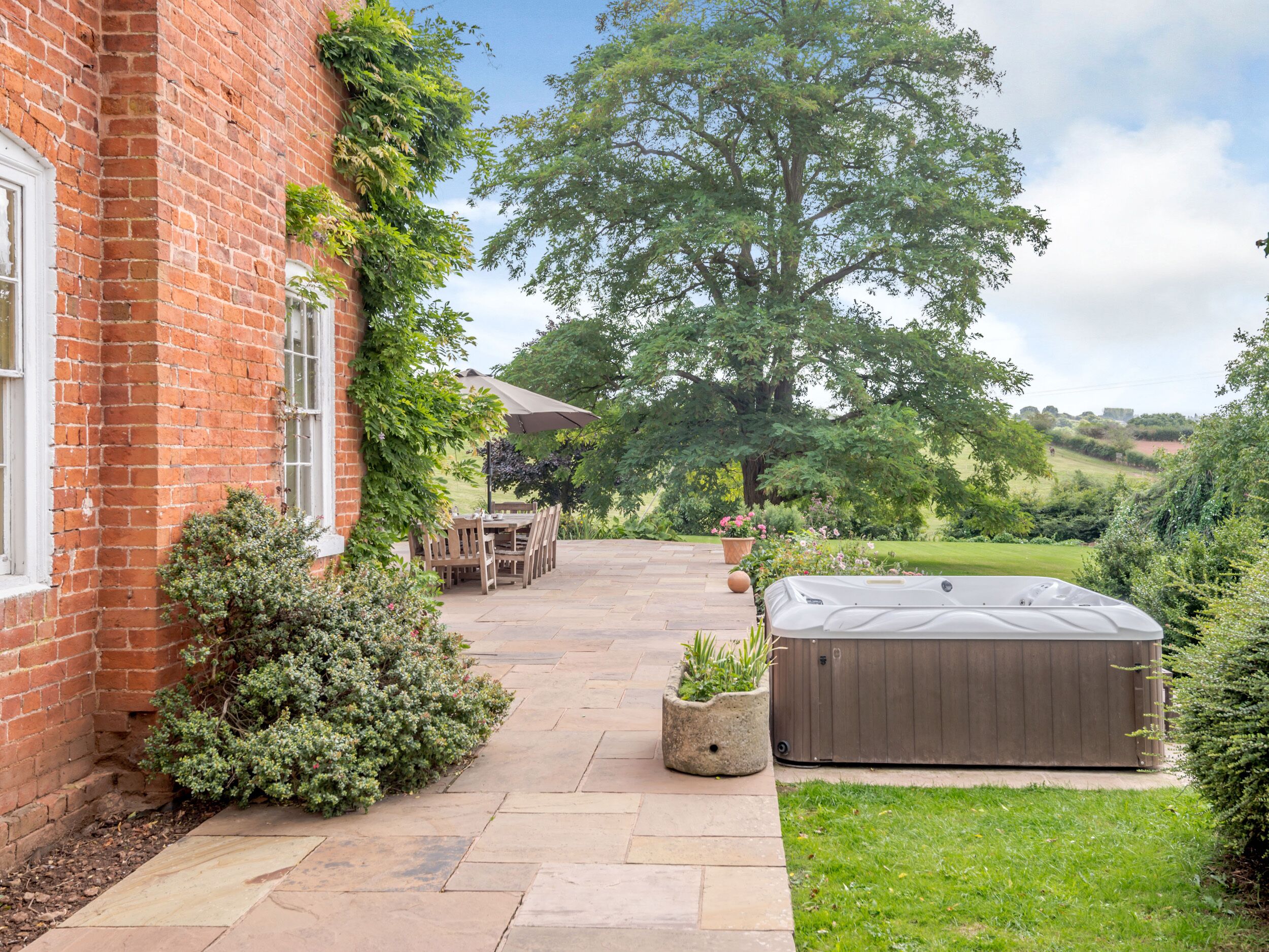 A brick house with a patio, a hot tub, and a lawn.