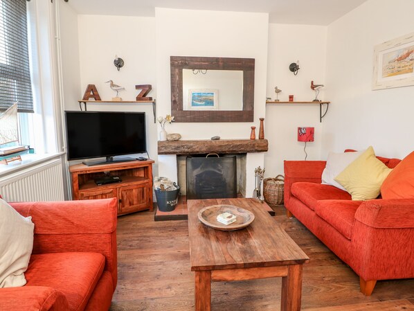 A living room with a television, red sofas, a wooden coffee table, a fireplace, and decorative items on the mantel.