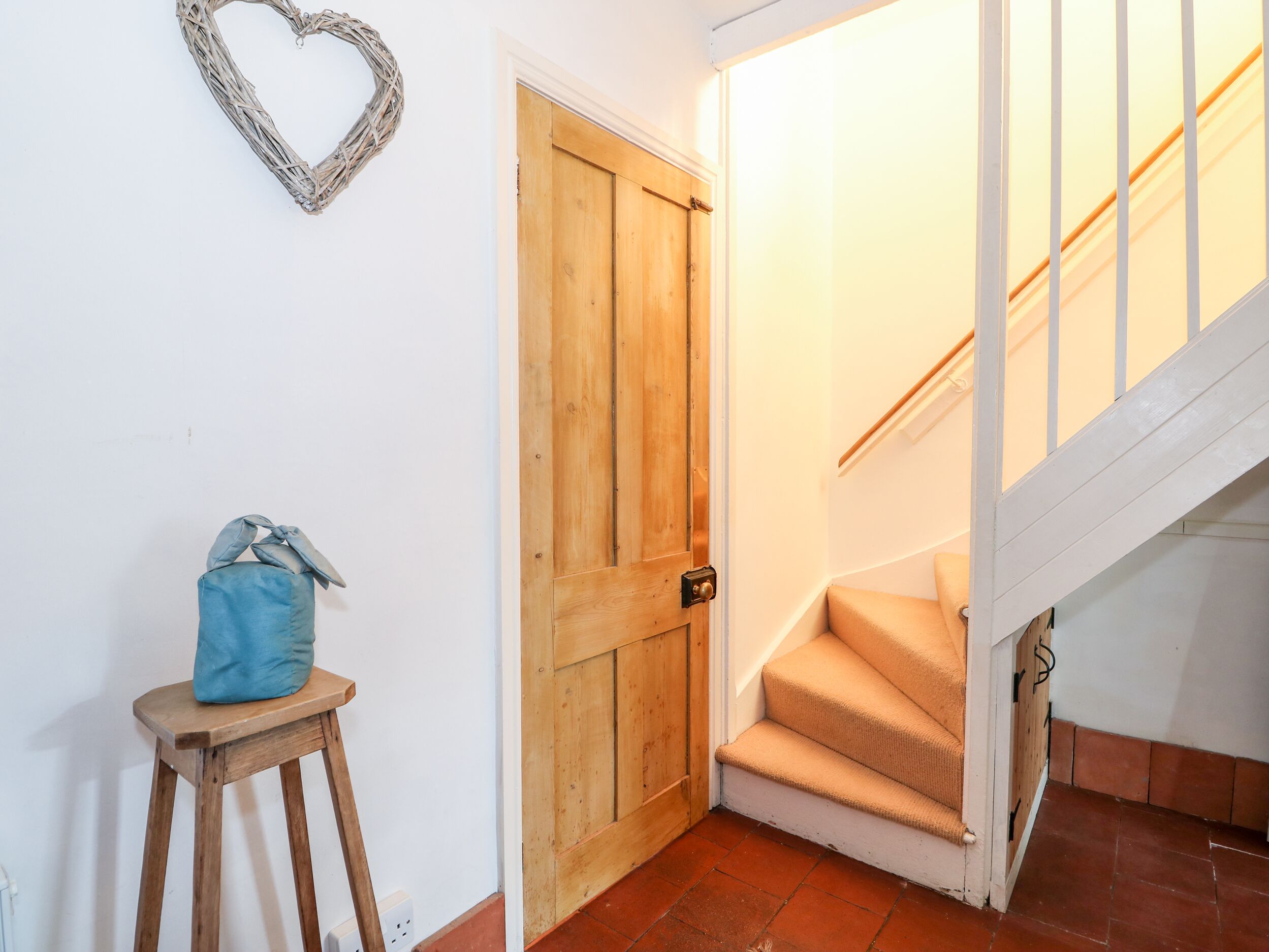 A wooden door, a heart-shaped decoration, a blue bag on a stool, and a staircase.