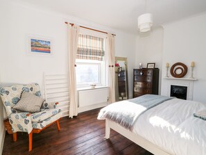 A bedroom with a bed, a chair, a dresser, a mirror, and a fireplace.
