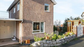 A two-story house with a stone facade, a garage, and a small garden with a stone wall and potted plants. - Bay View House (Colwyn Bay)