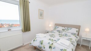 A bedroom with a bed, two bedside tables, a window with curtains, a radiator, and a framed picture on the wall. - Bay View House (Colwyn Bay)