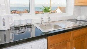 A modern kitchen with a view of the sea, a kettle, coffee makers, a sink, and a dishwasher. - Bay View House (Colwyn Bay)