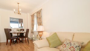 A living room with a beige sofa, a dining table with chairs, a chandelier, and a window with patterned curtains. - Bay View House (Colwyn Bay)