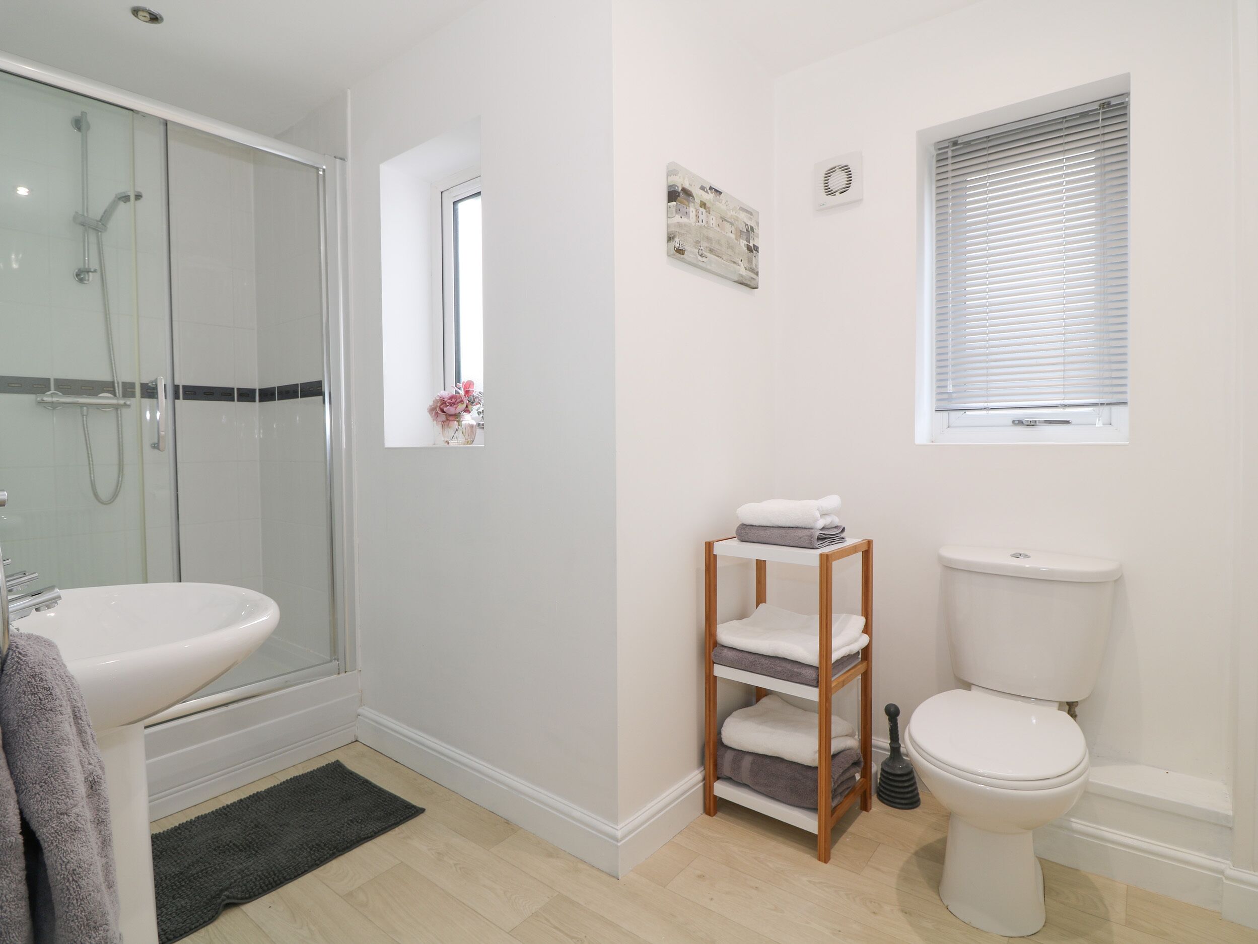 A bathroom with a shower, toilet, sink, and a small window.