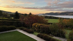 Un jardín ajardinado con un sendero, un césped y vistas a un lago y colinas a lo lejos.