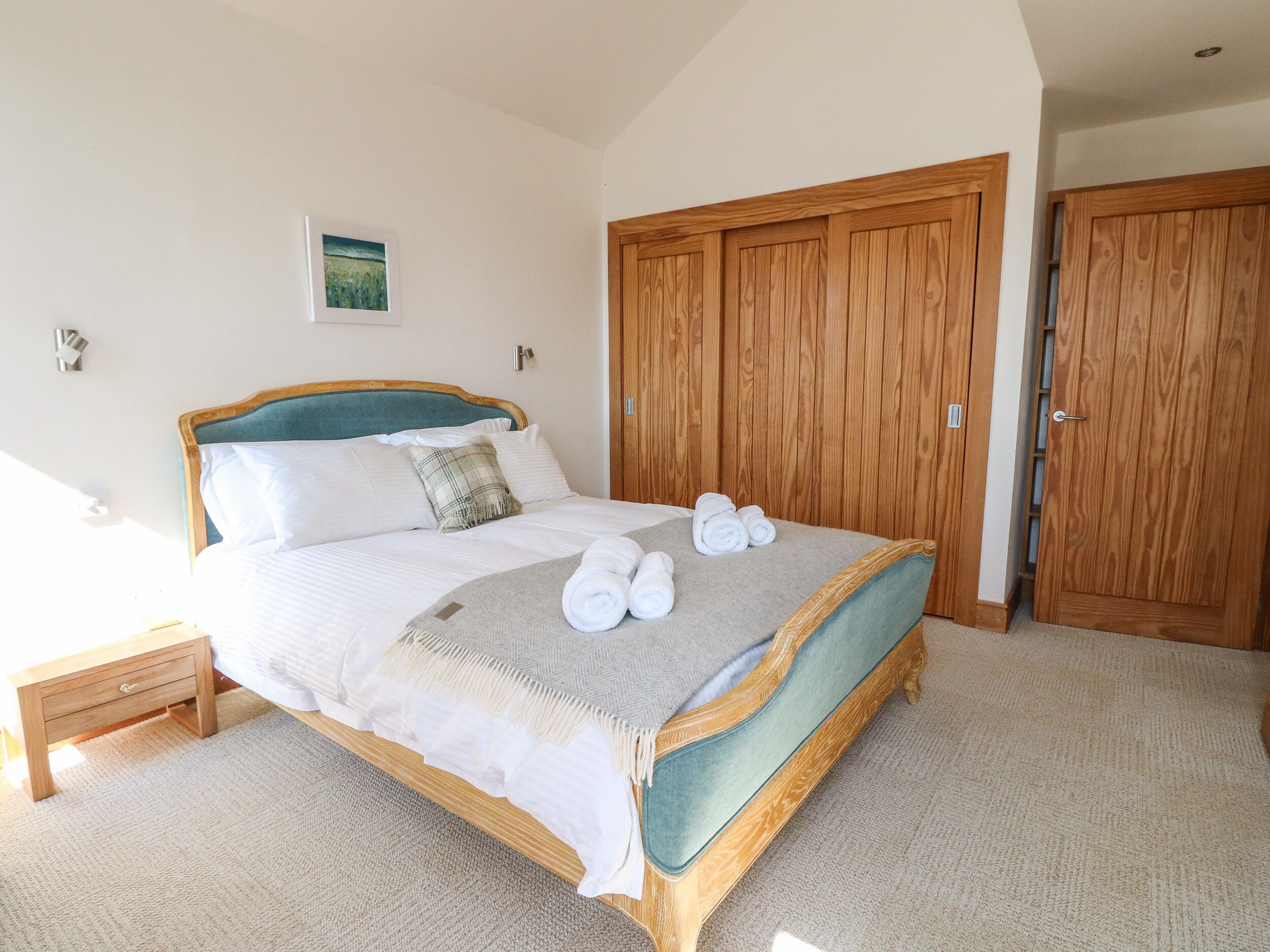 A bedroom with a bed, a nightstand, a wooden wardrobe, and a painting on the wall.