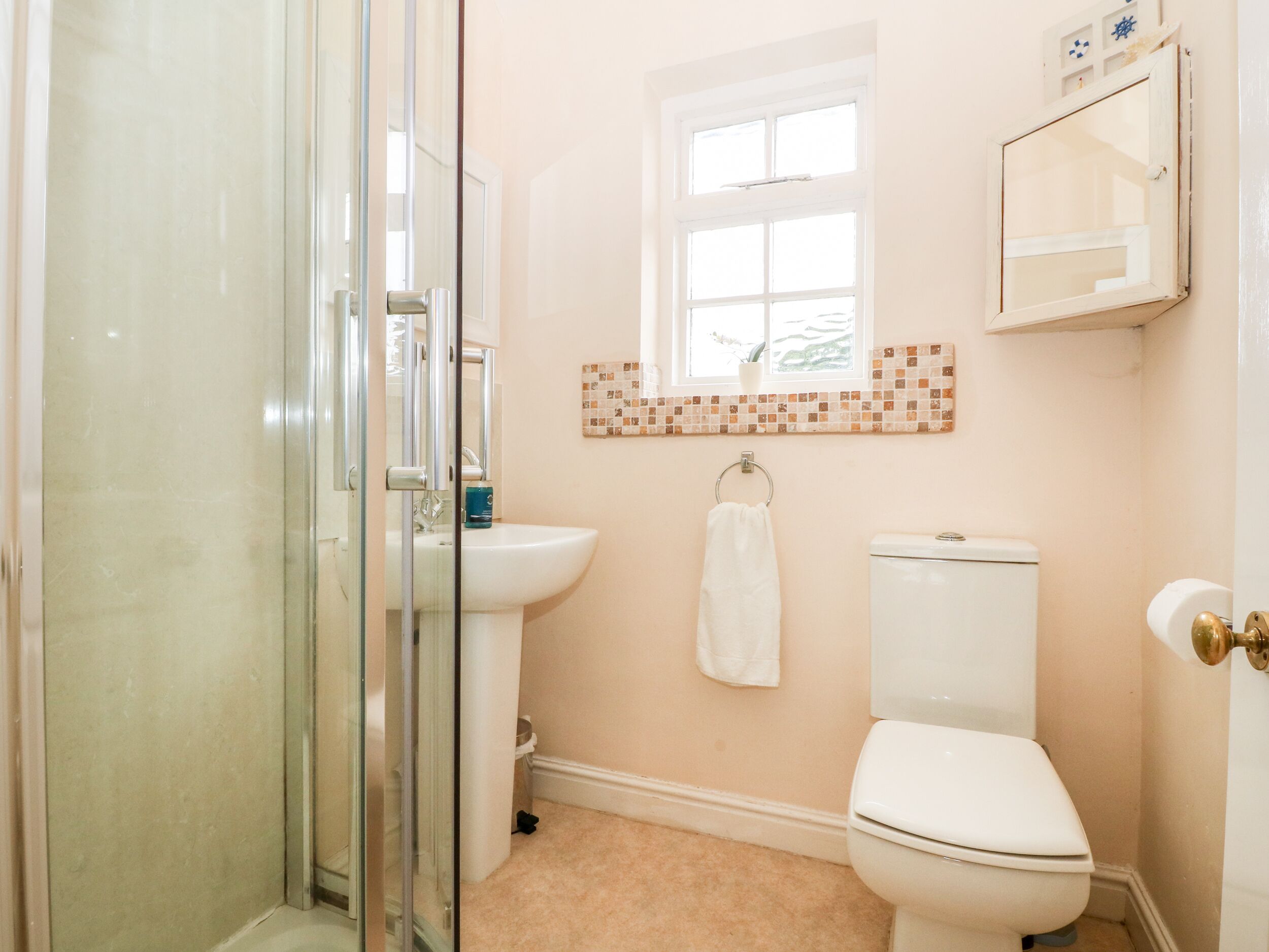 A bathroom with a glass shower enclosure, a sink, a toilet, and a window with a view of greenery.